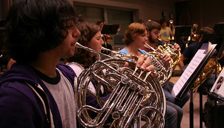 What makes the French horn a brass instrument, and what makes it